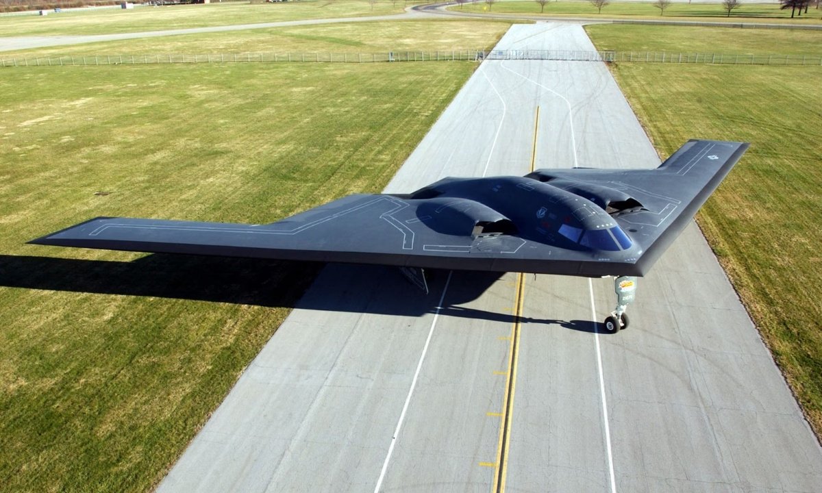 The Northrop B-2 Spirit stealth bomber on an airfield runway, seen from the front, showcasing its iconic flying wing design.