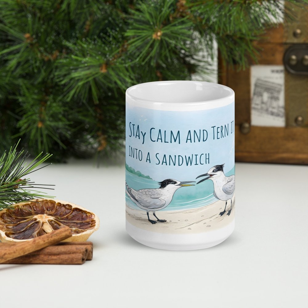White ceramic mug with watercolor Sandwich Terns and the quote ‘Stay calm and tern it into a sandwich,’ displayed on a holiday-themed table with greenery, dried citrus, and cinnamon sticks